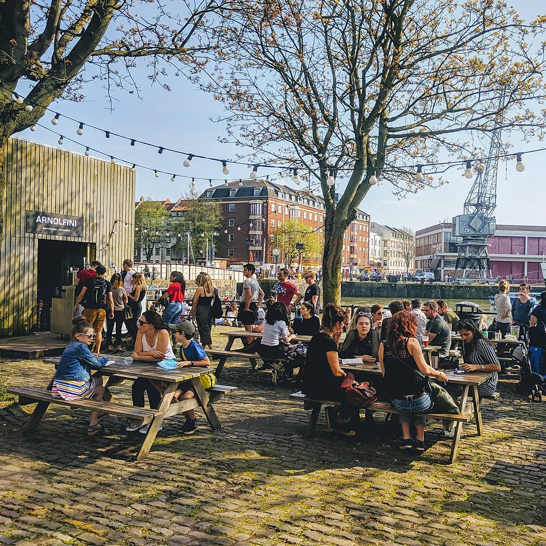 People eating at picnic benches on Bristol's harbourside by the Arnolfini
